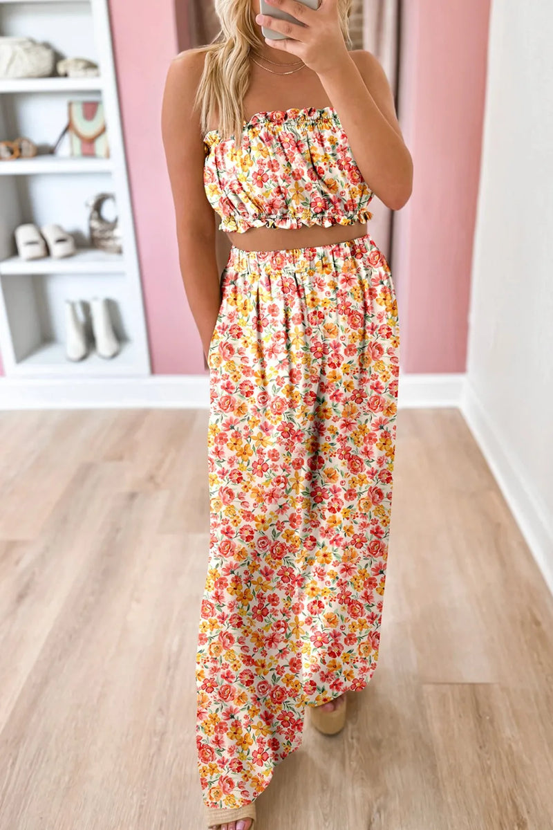 Woman wearing a floral two-piece outfit. The strapless top has elastic at top and bottom and shows the midriff, and the wide legged pants are high waisted, elastic topped as well.