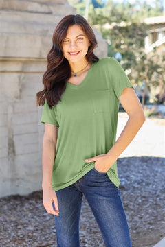 Woman wearing a green t-shirt and blue jeans standing outdoors.