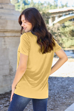 Woman wearing a yellow t-shirt and blue jeans standing outdoors.