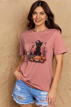 Pink t-shirt with a Halloween design featuring a black cat, pumpkins, leaves and bats in front of full orange moon.
