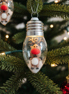Decorative light bulb with a reindeer figure inside hanging on a Christmas tree