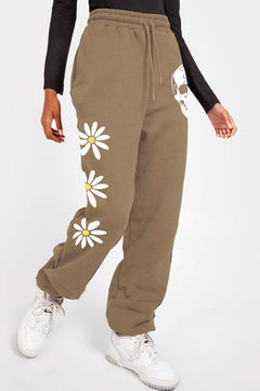 Khaki sweatpants with white skull partially obscured by daisys on left leg near the hip, and three large white daisys going down the other leg at thigh, knee and shin.
