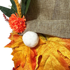 Decorative wreath with autumn leaves, flowers, and a white pom-pom on a plain background
