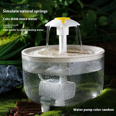 Cat water fountain with water flowing, surrounded by greenery clear bowl with white fountain head shaped like a daisy. Lettering on pic says simulate natural springs  cats drink more water compared to a still water bowl cats prefer to drink running water