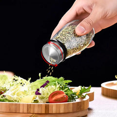 Hand sprinkling dried herbs from a shaker onto a salad on a wooden board.