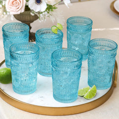 Set of blue glass tumblers on a marble tray with limes and flowers in the background
