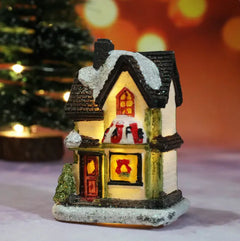 Decorative miniature house with glowing interior lights on a blurred Christmas tree background