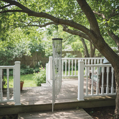 Decorative wind chime hanging from a shady tree near an outdoor sitting area