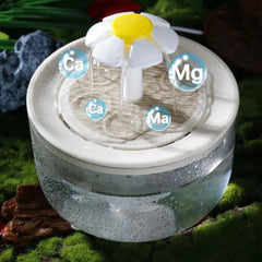 Cat water fountain with water flowing, surrounded by greenery clear bowl with white fountain head shaped like a daisy. 