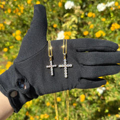 Gold vermeil cross pendant necklaces with moissanite stones laid across the palm of a black gloved hand to show the sparkle with sunlight hits it