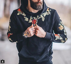 Man wearing a black hoodie with floral embroidery on a blurred background