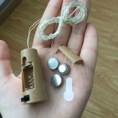 Hand holding a beige hearing aid, batteries, and screws on a wooden surface