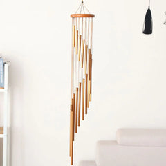 Gold metal and wood wind chime hanging in a room with a white wall and light-colored furniture.