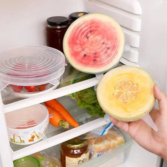 Person holding a sliced watermelon in front of a refrigerator with food items.