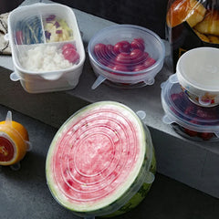 Close-up of a sliced watermelon with a lid on a table, surrounded by other containers.