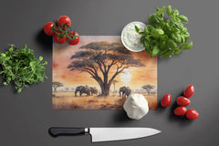 Glass cutting board with an African landscape design, surrounded by vegetables and a knife on a dark surface.