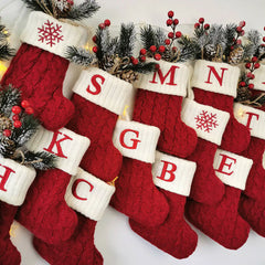Red Christmas stockings style crew socks with snowflake and letter design, surrounded by festive decorations.