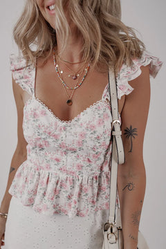 Woman wearing a floral top with ruffled details and a white skirt, holding a beige handbag.