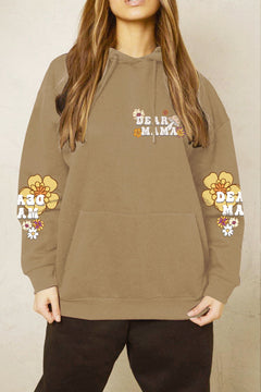 Person wearing a brown hoodie with 'DEAR MAMA' text and floral designs on a beige background