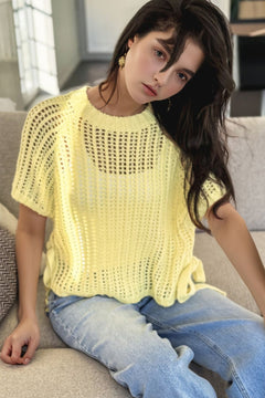 Woman wearing a yellow crochet beach cover up and blue jeans sitting on a couch.