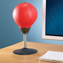 Red desk punching bag on a wooden desk with a computer monitor in the background.