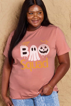 Pink round neck tshirt with short sleeves. Hallowee Theme with the word Boo but the first o is a sheet ghost and the second o is a white jack o'lantern and below that is the word Squad in orange. Above the B is an orange spider web and above the pumpkin are three orange flying bat silhouttes