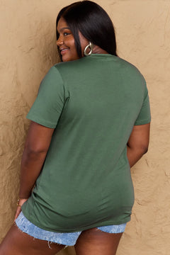 Woman wearing a green t-shirt and denim shorts against a beige wall