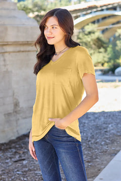 Woman wearing a yellow top and blue jeans standing outdoors with a blurred background