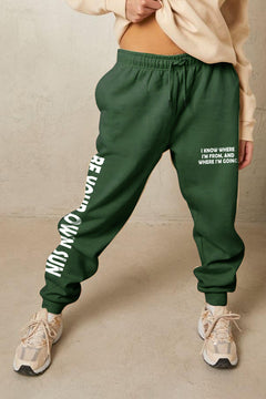 Forrest Green sweatpants with elastic waist and drawstring, cuffed legs and side pockets. Left leg says on the thigh I know where I'm From and Where I'm Going. Down the right leg it says BE YOUR OWN SUN