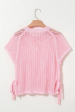 Pink crochet top on a hanger against a white background