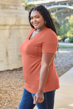 Woman wearing an orange shirt and blue jeans standing outdoors with a bridge in the background