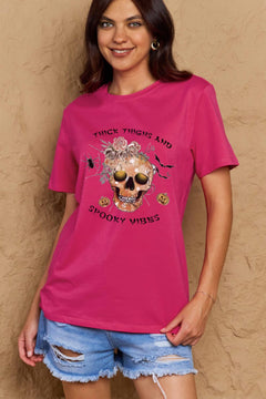 Pink t-shirt with a skull surrounded by small Jackolanterns, batts, flowers and a spider. The text Reads Thick Thighs and Spooky Vibes