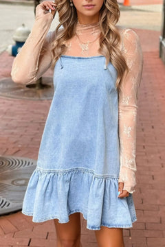 Woman wearing a light blue denim dress with sheer sleeves on a brick pavement.