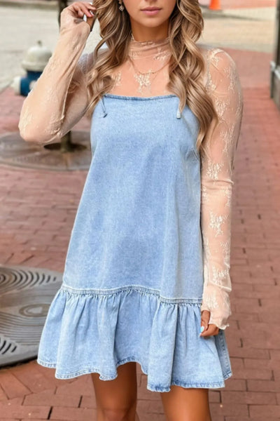 Woman wearing a light blue denim dress with sheer sleeves on a brick pavement.
