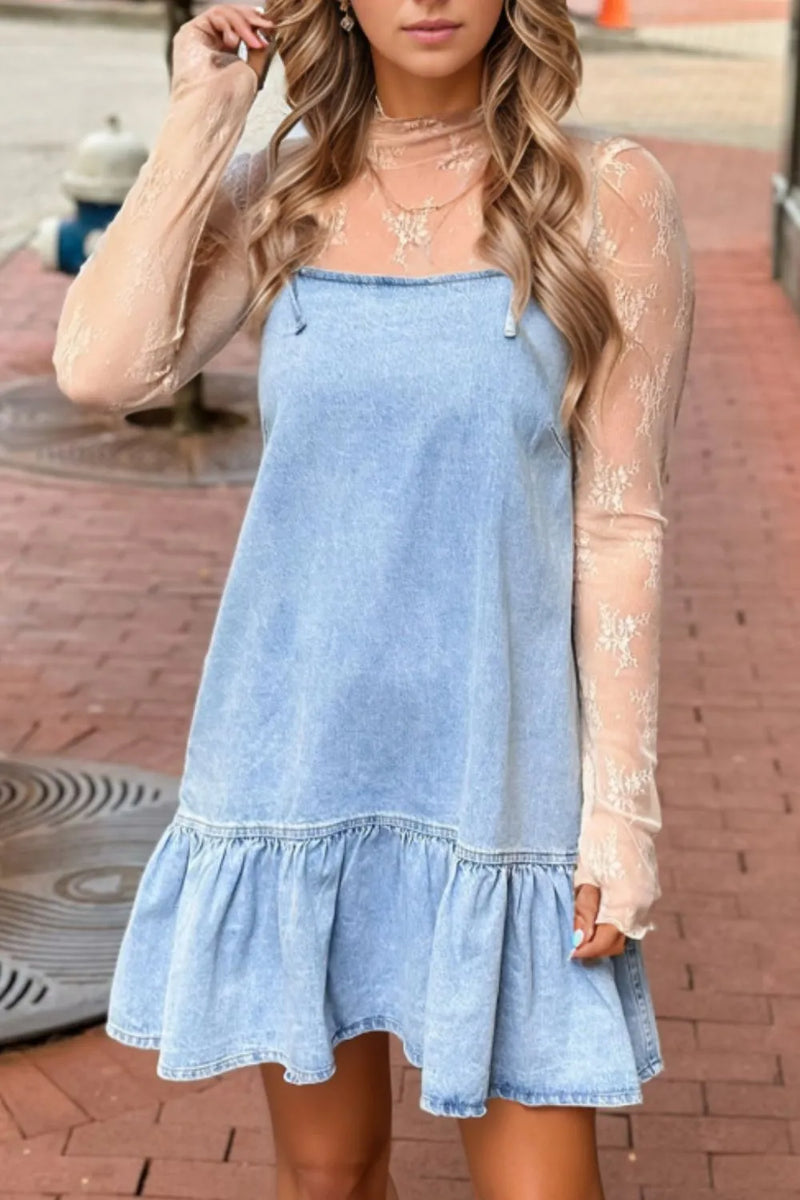 Woman wearing a light blue denim dress with sheer sleeves on a brick pavement.