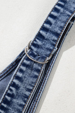 Close-up of a blue denim overall strap with a metal buckle on a light gray background