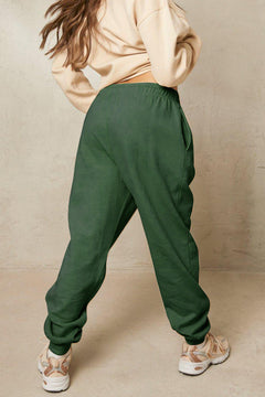 Person wearing green pants and a beige top against a beige background