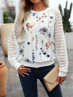 Woman wearing a floral sweater with lace sleeves and holding a beige clutch.
