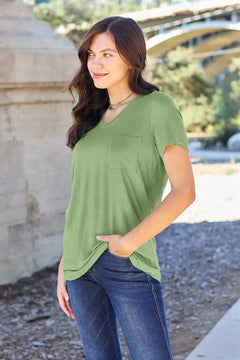 Woman wearing a green shirt and blue jeans standing outdoors with a blurred background