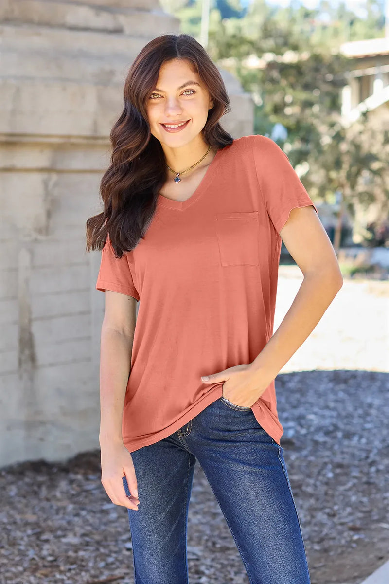 Woman wearing a terracotta-colored t-shirt and blue jeans standing outdoors.