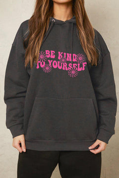 A black hoodie with pink block letters stating BE KIND TO YOURSELF with pink flowers around the words.Handwarmer pocket on front, pullover