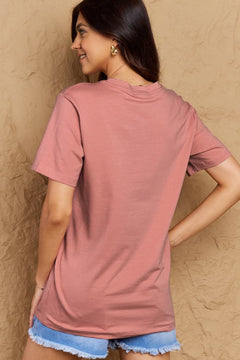 Woman wearing a pink t-shirt and denim shorts against a beige wall