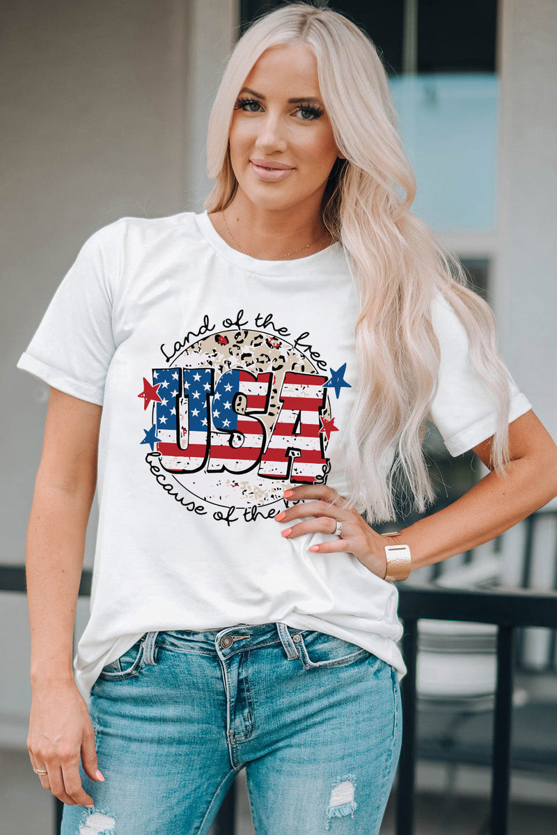 white short sleeved tshirt with USA designed like an American Flag in front of a circle that has flowers in it and the words Land of the Free because of the brave in cursive curving around the design