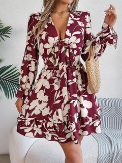 Woman wearing a burgundy and white floral dress holding a straw bag indoors.