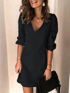 Woman wearing a black dress holding a black clutch against a neutral background