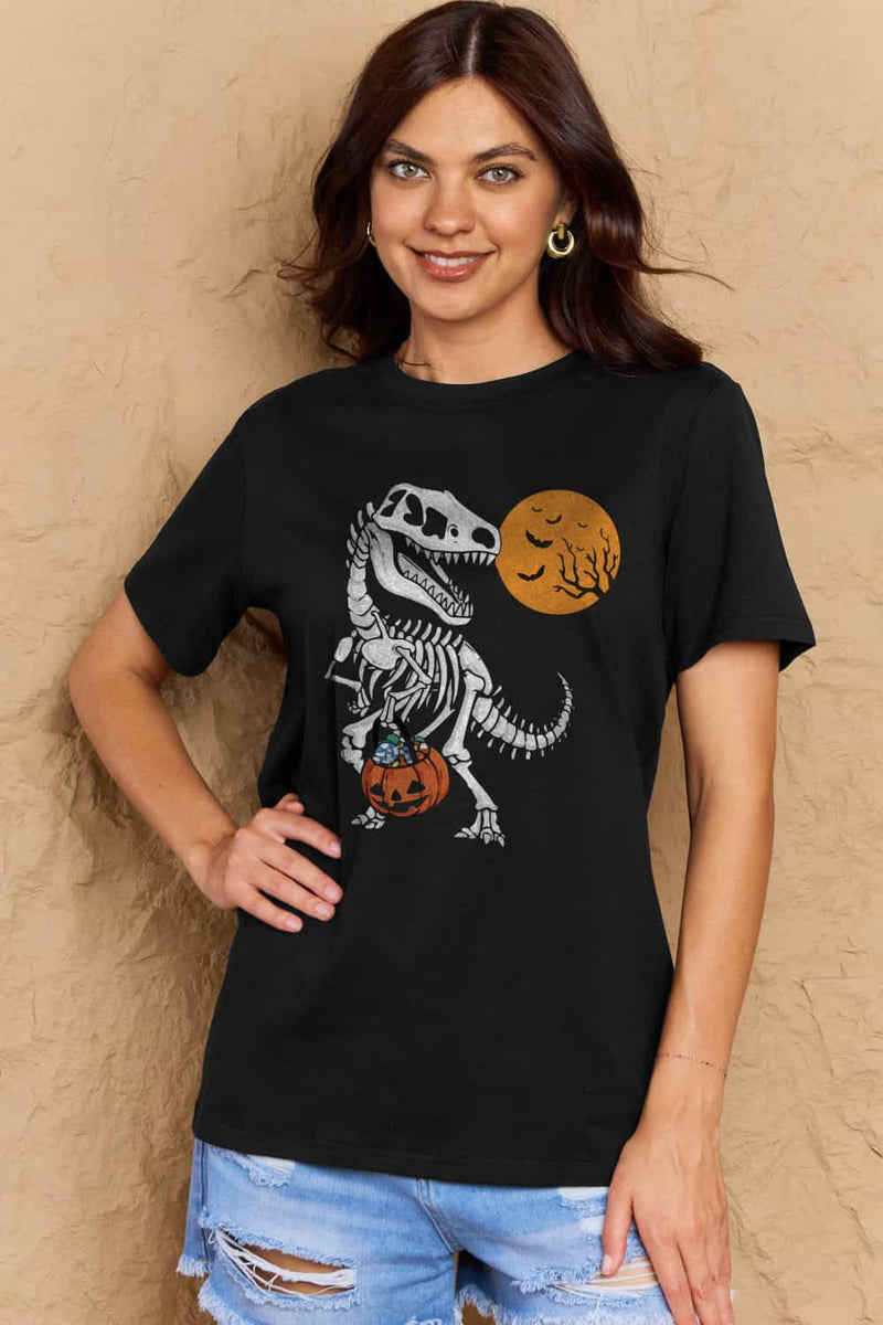 black short sleeved t-shirt with a dinosaur skeleton design on front. Dinosaur is holding a trick or treat jack o'lantern basket with candy in it and looking back at an orange moon with the silhouttes of bats and tree branches in front of it