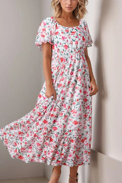 Floral Short Puff Sleeve Tiered Dress with wide round neck and high waist. White background with different sizes and types of pink flowers all over it. Some dark pink and some light, some in full bloom, some budding out. Green leaves and stems.