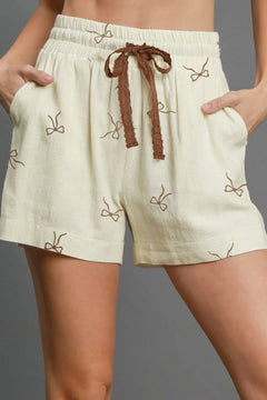 Beige shorts with brown drawstring and bow patterns on a gray background
