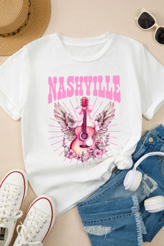 Creamy white Tshirt with short sleeves and round neck, the design is a Guitar standing on end, with the arm pointing up. There is a pink bow tied towards the top with long ribbon ends flowing down, pink and white wings extend out behind the guitar and the bottom is nestled in pink flowers that look similar to a carolina rose.Extending out all around the design are straight pink lines which imply rays of light. The caption above the design is in Pink Capital letters and says NASHVILLE
