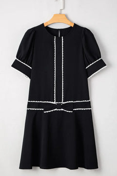 Black dress with white trim on a hanger against a white background